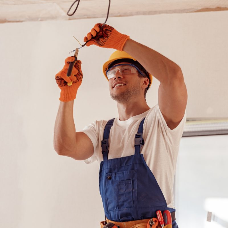 Cheerful electrician repairing electric cable on ceiling