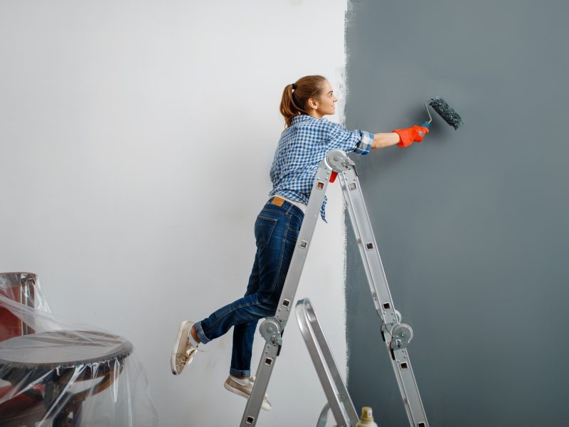 Female house painter in gloves paints the wall