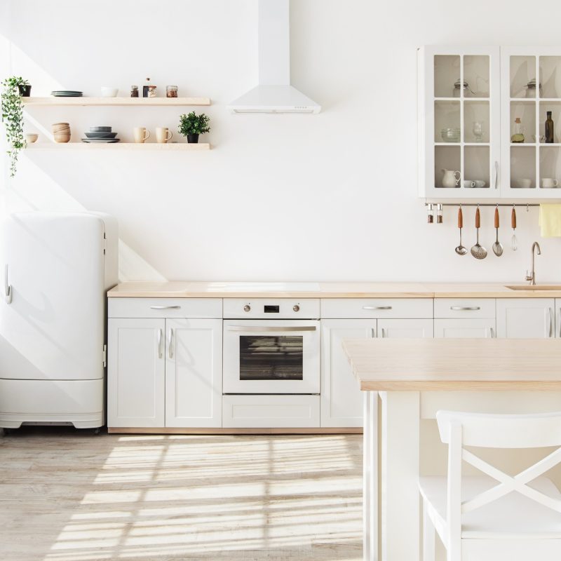 Light kitchen interior with white furniture and shelves, small refrigerator near window, empty space