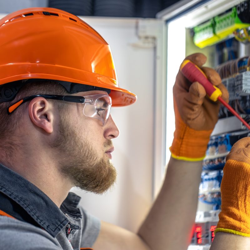 Male electrician working in switchboard. Male electrician in overalls working with electricity.